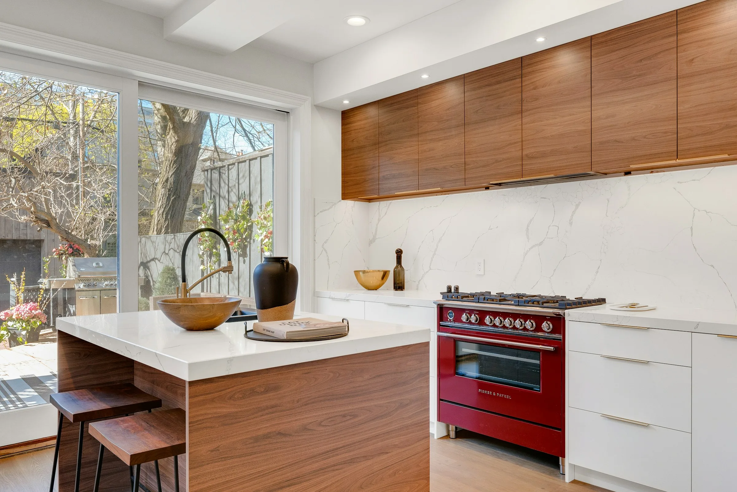 Walnut upper cabinetry above a white island, garden window and range